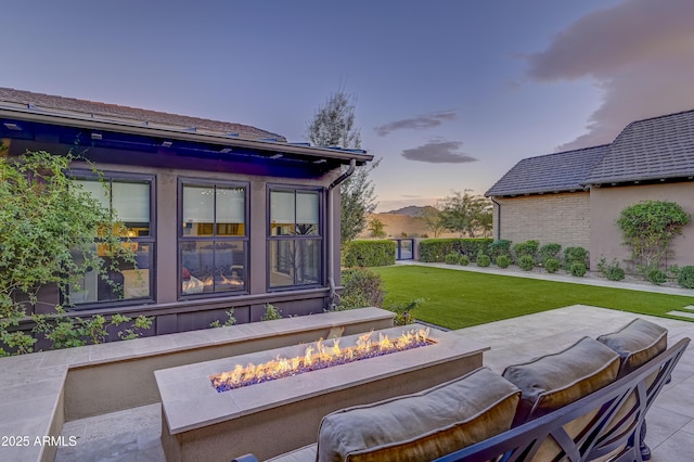 patio terrace at dusk featuring a yard and a fire pit