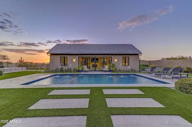 pool at dusk featuring a yard, a patio area, pool water feature, and an outbuilding