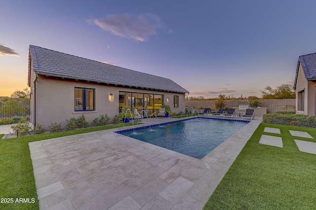 pool at dusk with pool water feature, a patio area, and a lawn