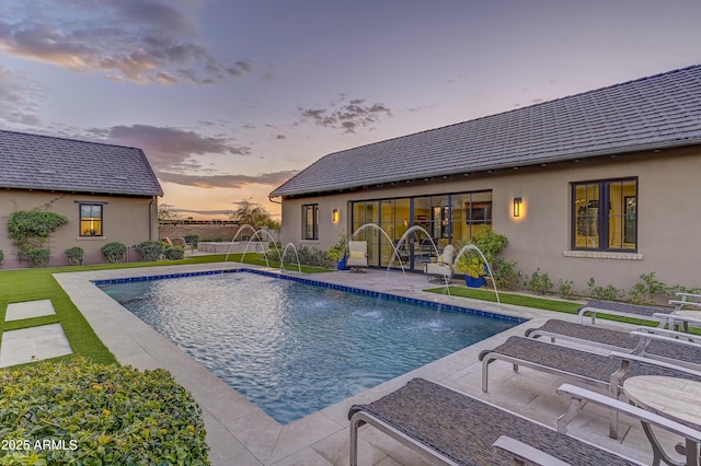 pool at dusk with pool water feature and a patio