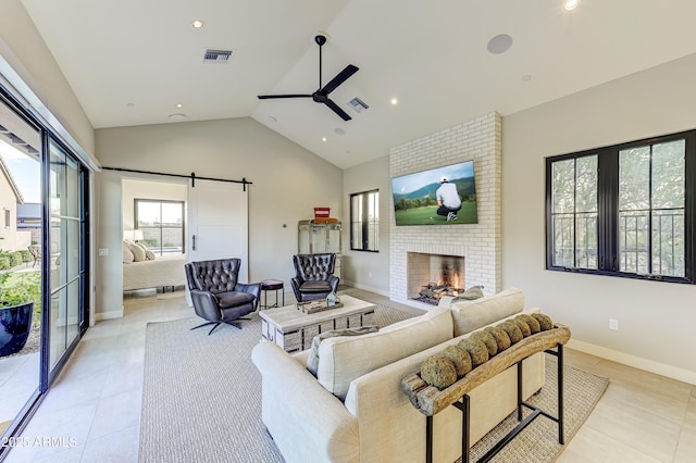 living room with a brick fireplace, vaulted ceiling, ceiling fan, light tile patterned floors, and a barn door