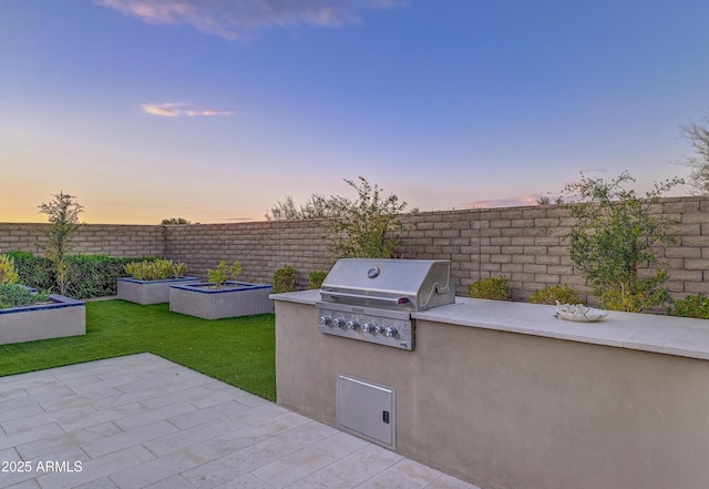 patio terrace at dusk with exterior kitchen, a yard, and grilling area