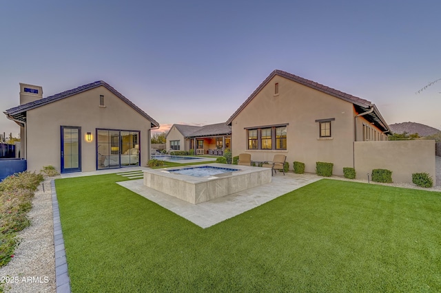 back house at dusk with an in ground hot tub, a yard, and a patio