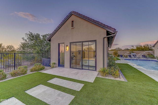 back house at dusk with pool water feature, a fenced in pool, a patio, and a lawn