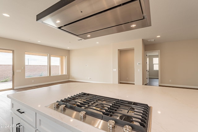 details featuring stainless steel gas stovetop, white cabinets, light hardwood / wood-style flooring, light stone countertops, and extractor fan