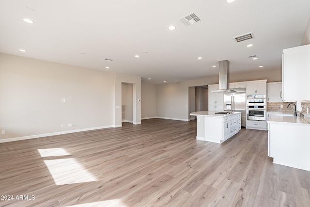 kitchen with island exhaust hood, stainless steel gas cooktop, white cabinets, a center island, and light hardwood / wood-style floors