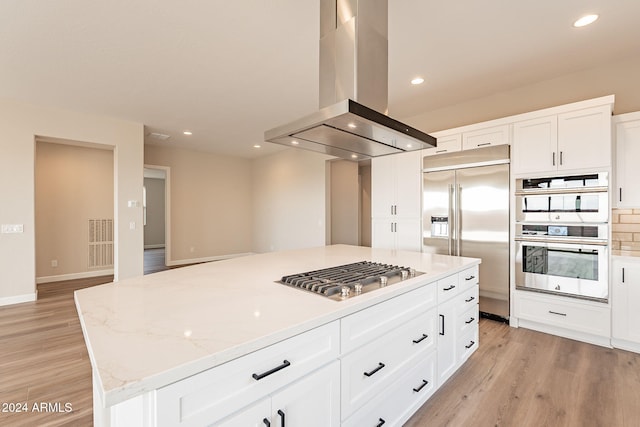 kitchen featuring light stone countertops, a kitchen island, island range hood, white cabinets, and appliances with stainless steel finishes