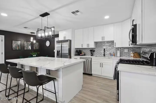 kitchen with white cabinets, sink, light hardwood / wood-style floors, a kitchen island, and stainless steel appliances