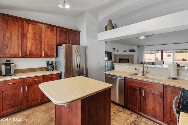 kitchen featuring a tiled fireplace, stainless steel appliances, sink, vaulted ceiling, and a center island