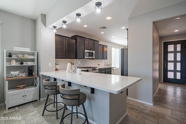 kitchen with appliances with stainless steel finishes, sink, a breakfast bar area, backsplash, and kitchen peninsula