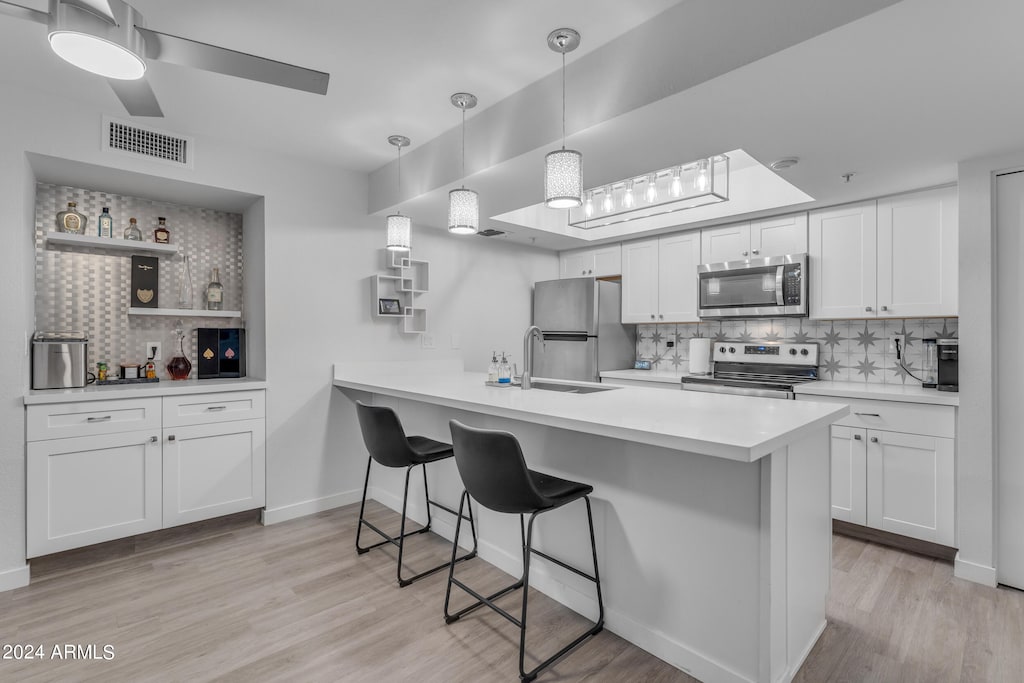 kitchen featuring light wood finished floors, visible vents, a breakfast bar area, appliances with stainless steel finishes, and a peninsula