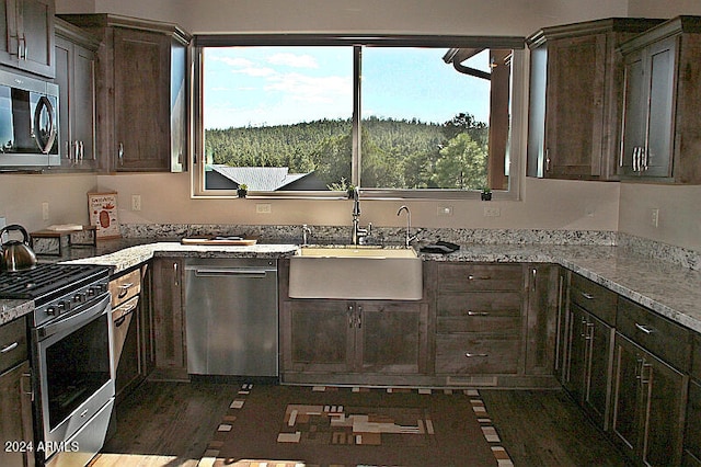 kitchen with appliances with stainless steel finishes, dark wood-type flooring, light stone counters, dark brown cabinets, and sink