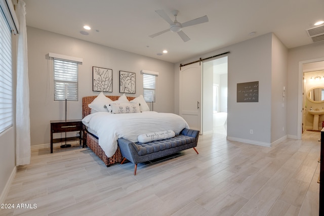 bedroom with light wood-type flooring, ceiling fan, a barn door, and connected bathroom