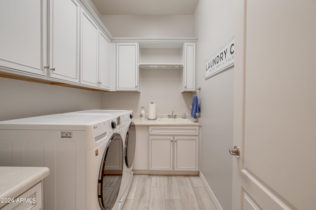 clothes washing area featuring cabinets, washing machine and clothes dryer, sink, and light hardwood / wood-style floors