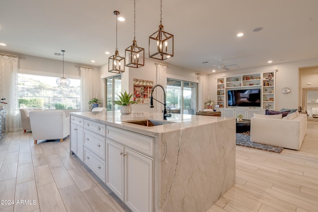 kitchen with light stone counters, white cabinetry, sink, pendant lighting, and a kitchen island with sink