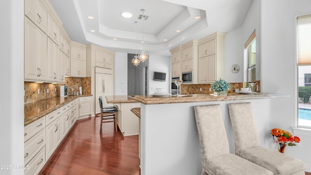 3126 E Fruitvale Ct, Gilbert, AZ 85297 - kitchen with built in appliances, cream cabinetry, a peninsula, dark wood-style floors, and decorative backsplash