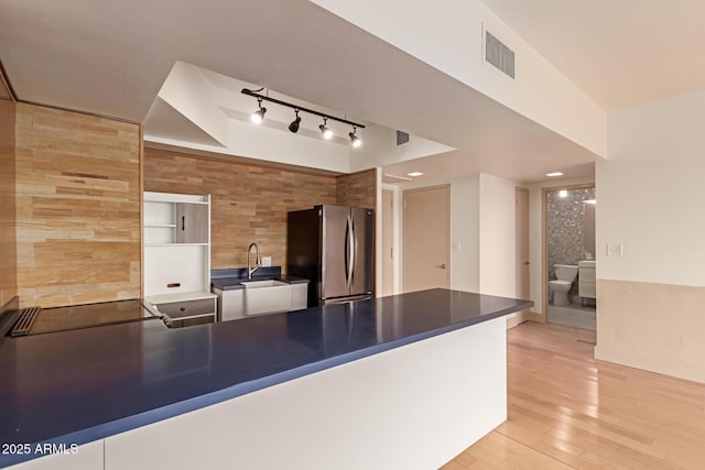 kitchen with stainless steel refrigerator, wood walls, sink, light hardwood / wood-style floors, and black electric cooktop