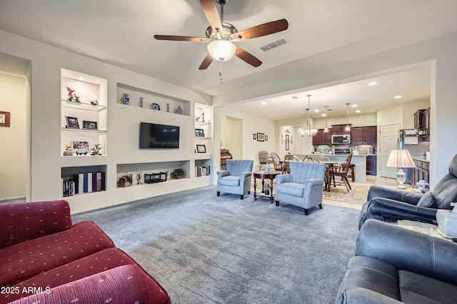 living room featuring ceiling fan with notable chandelier and built in features