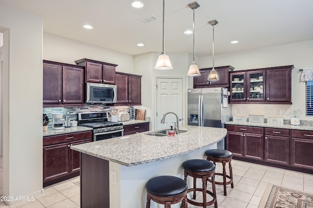 kitchen with stainless steel appliances, sink, a breakfast bar, light tile patterned floors, and a center island with sink