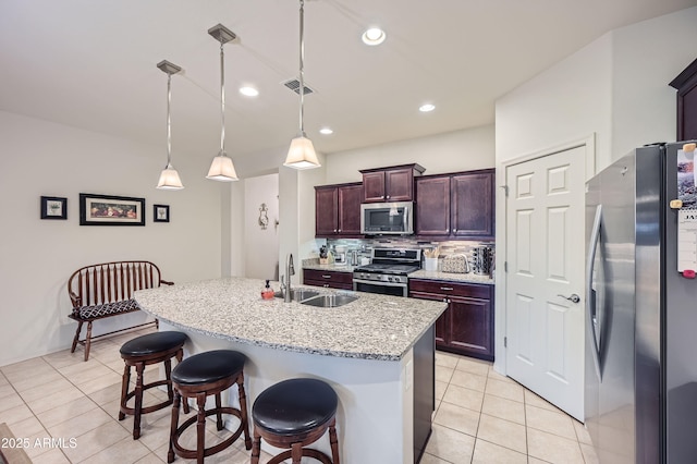 kitchen with decorative light fixtures, stainless steel appliances, decorative backsplash, sink, and a center island with sink