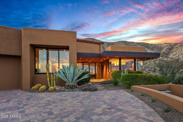 back of property at dusk featuring stucco siding, a mountain view, and an attached garage
