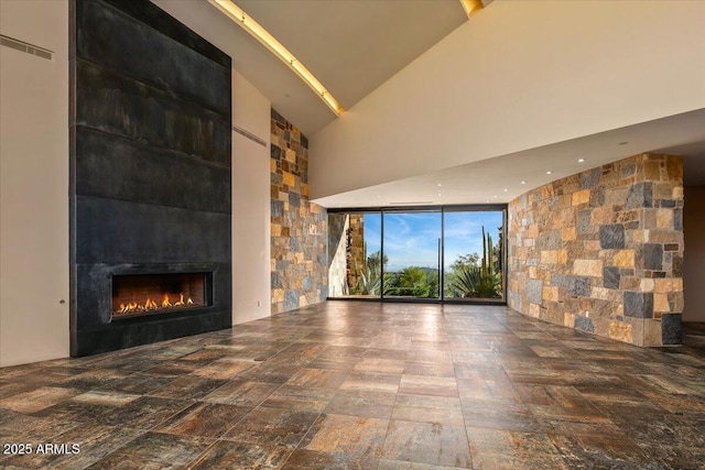 unfurnished living room with a large fireplace, a high ceiling, and floor to ceiling windows