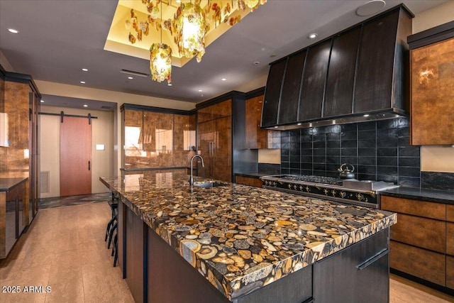 kitchen with custom exhaust hood, a barn door, a sink, range with gas stovetop, and decorative backsplash