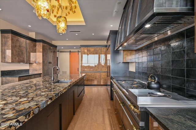 kitchen with tasteful backsplash, dark stone countertops, a barn door, a sink, and light wood-style flooring