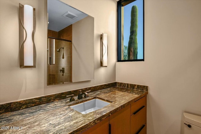 bathroom with toilet, tiled shower, vanity, and visible vents