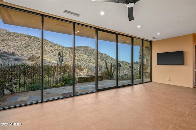 unfurnished living room featuring visible vents, a wall of windows, a ceiling fan, and tile patterned flooring