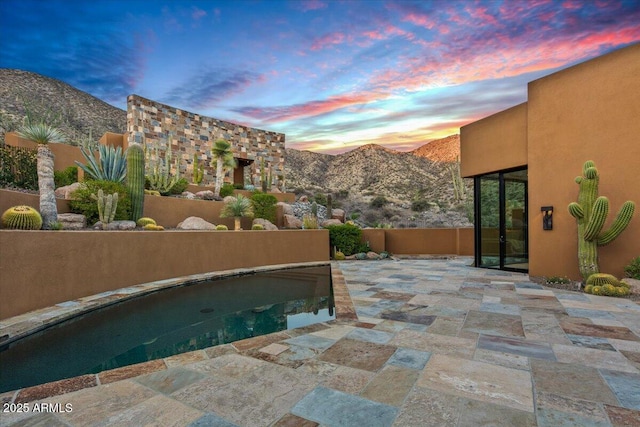 pool at dusk featuring a mountain view, a patio, and a pool