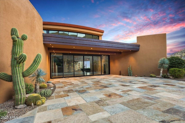 back of house at dusk featuring a patio area and stucco siding