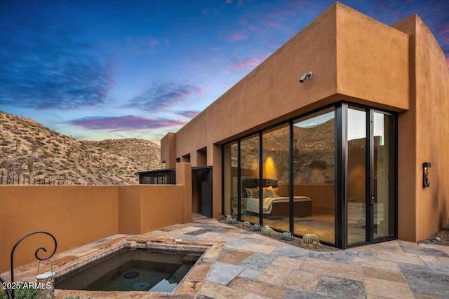 exterior space featuring an in ground hot tub, a patio, and stucco siding