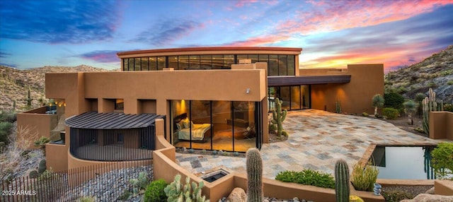 back of property at dusk featuring a mountain view, a standing seam roof, and stucco siding