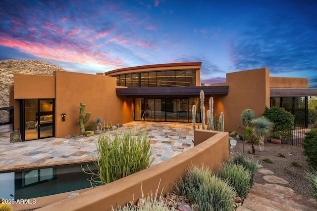 back of house at dusk with a patio, stucco siding, and fence