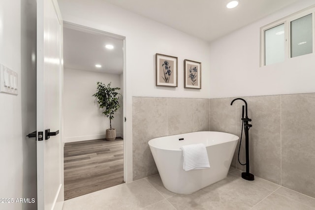 bathroom with tile walls, a tub to relax in, and tile patterned floors