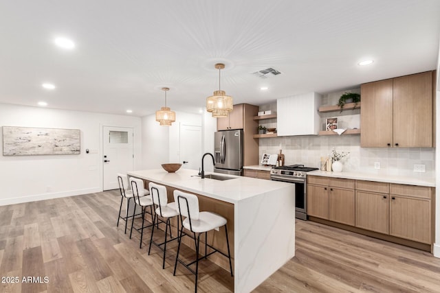 kitchen with sink, tasteful backsplash, a kitchen island with sink, stainless steel appliances, and light hardwood / wood-style floors