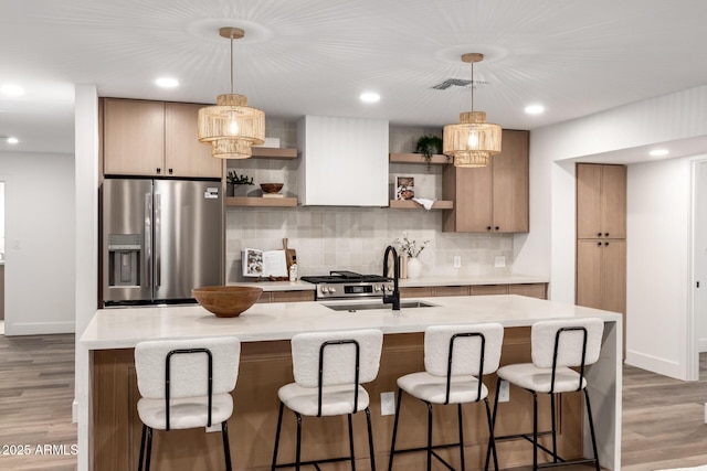 kitchen featuring an island with sink, stainless steel fridge, sink, and hanging light fixtures