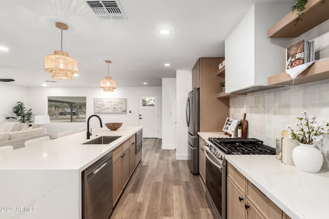 kitchen featuring appliances with stainless steel finishes, tasteful backsplash, sink, hanging light fixtures, and light hardwood / wood-style flooring