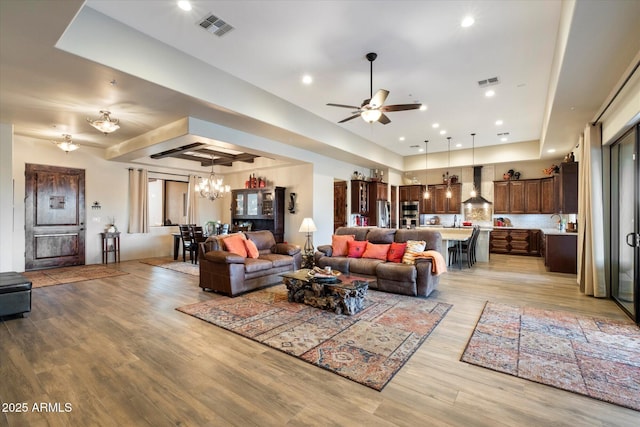 living room featuring ceiling fan with notable chandelier and light hardwood / wood-style flooring