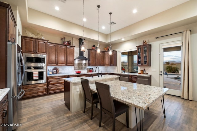 kitchen featuring stainless steel appliances, a center island with sink, a kitchen breakfast bar, and wall chimney exhaust hood