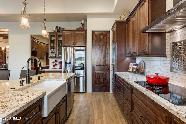 kitchen with wall chimney exhaust hood, hanging light fixtures, light hardwood / wood-style flooring, stainless steel appliances, and decorative backsplash