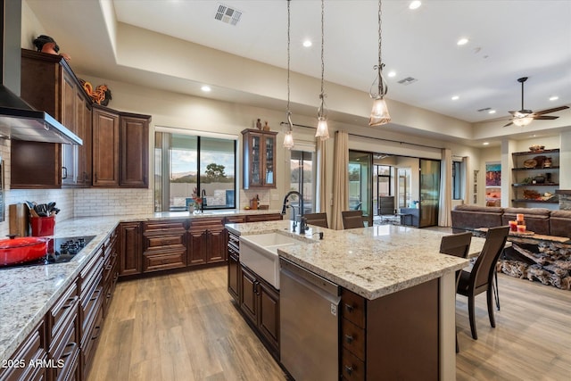 kitchen with dishwasher, sink, a kitchen bar, black electric stovetop, and a center island with sink