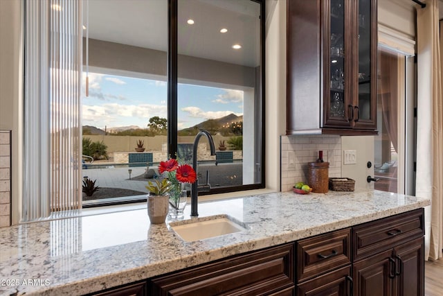 kitchen featuring tasteful backsplash, dark brown cabinetry, light stone countertops, and sink