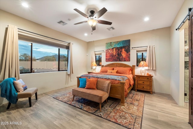 bedroom featuring a barn door, ceiling fan, and light hardwood / wood-style flooring