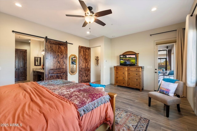 bedroom with ensuite bathroom, a barn door, wood-type flooring, ceiling fan, and access to exterior