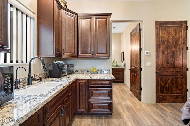 kitchen featuring light stone counters, sink, dark brown cabinetry, and light wood-type flooring