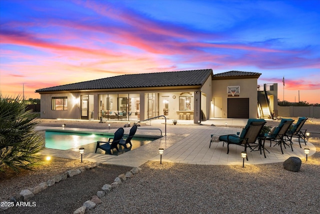 back house at dusk featuring a fenced in pool and a patio area