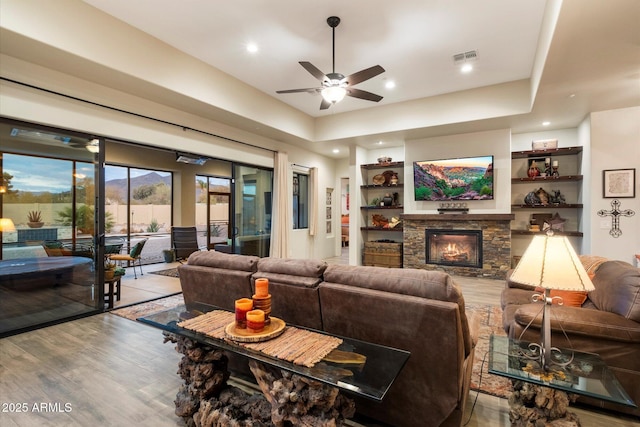 living room featuring a stone fireplace, ceiling fan, and light wood-type flooring