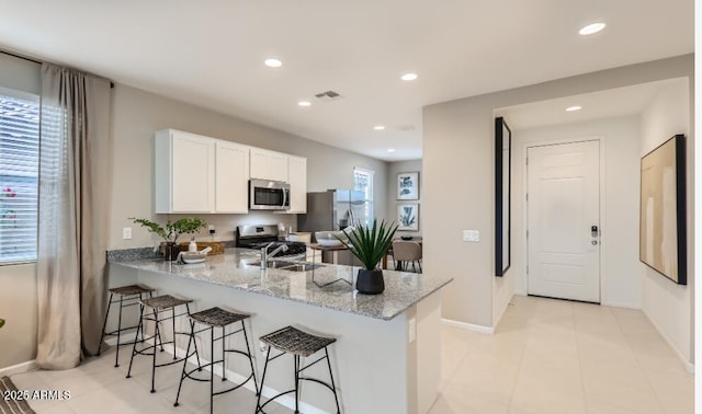 kitchen featuring appliances with stainless steel finishes, a breakfast bar, white cabinetry, kitchen peninsula, and light stone countertops